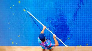 a man using a net to remove leaves from a pool